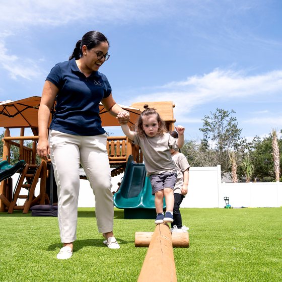 A child walking a balance beam with a teacher's help
